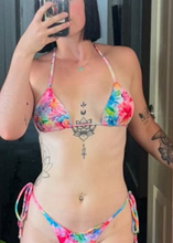 Load image into Gallery viewer, Person wearing a colorful tie-dye bikini with tattoos visible on arms and chest.
