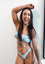 Load image into Gallery viewer, Woman wearing a blue floral bikini with tattoos on her arms, standing indoors.