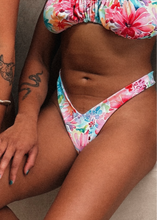 Load image into Gallery viewer, Two individuals wearing floralMiami V Cut Cheeky Bikini Bottoms in multicolor floral print. The image focuses on the bikini bottoms and the legs of the wearers, showcasing the high cut design and cheeky cut.