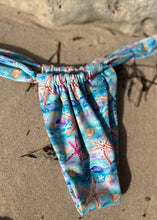 Load image into Gallery viewer, Colorful bikini bottom with starfish and shell pattern on sandy surface
