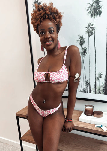 Woman in a pink bikini standing in a room with a wooden shelf and framed picture.