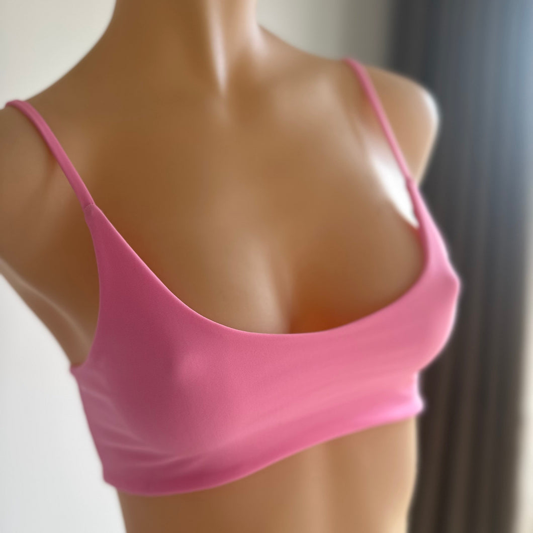 A pink bralette top displayed on a mannequin, featuring thin straps and a removable bow tie at the front.