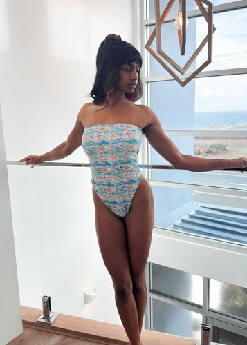 Woman in a floral swimsuit standing by a large window with a cityscape view.
