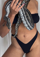 Load image into Gallery viewer, A woman wearing a black bikini holds a large black and white patterned snake draped over her shoulders and across her torso against a light curtain background.
