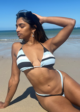 Load image into Gallery viewer, Woman in a black and white striped bikini sitting on a beach.
